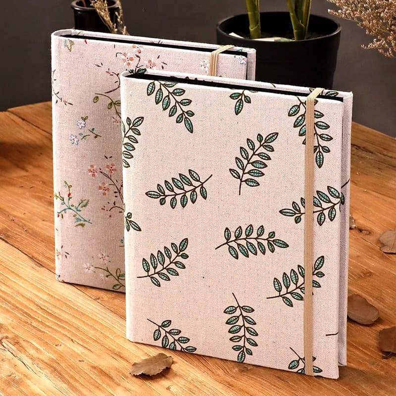 Deux albums de scrapbooking à couverture en toile rose imprimée de feuillages, posés debout sur une table en bois.