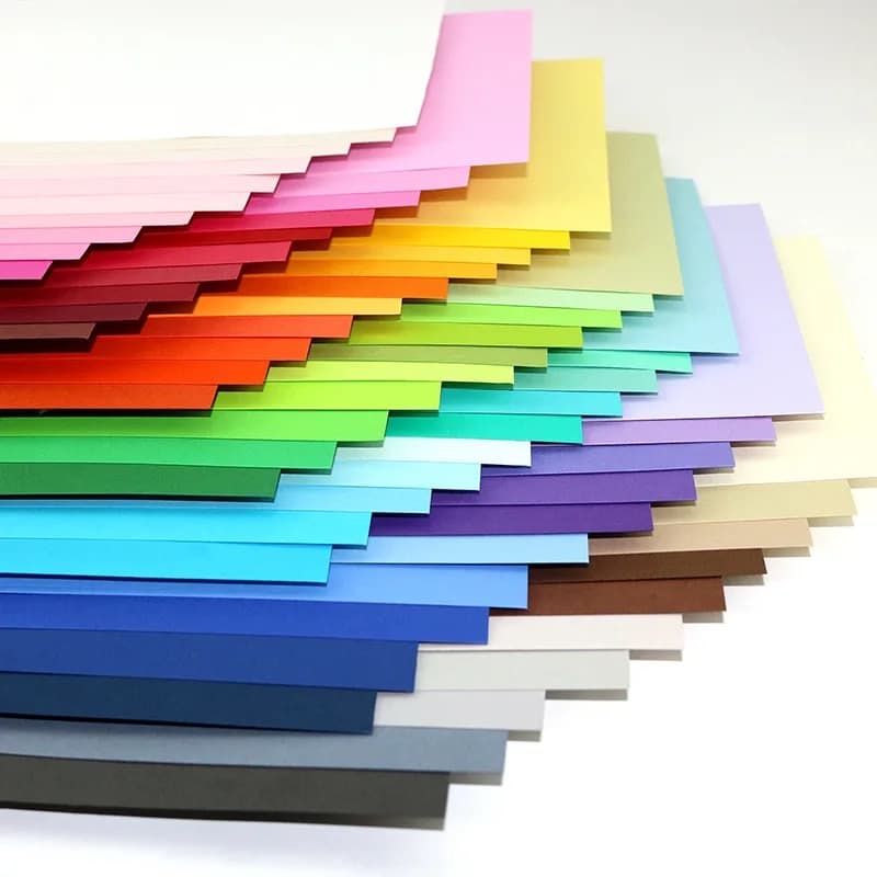 Feuilles de cardstock disposées en éventail montrant une trentaine de couleurs, du rose au gris anthracite, sur fond blanc.