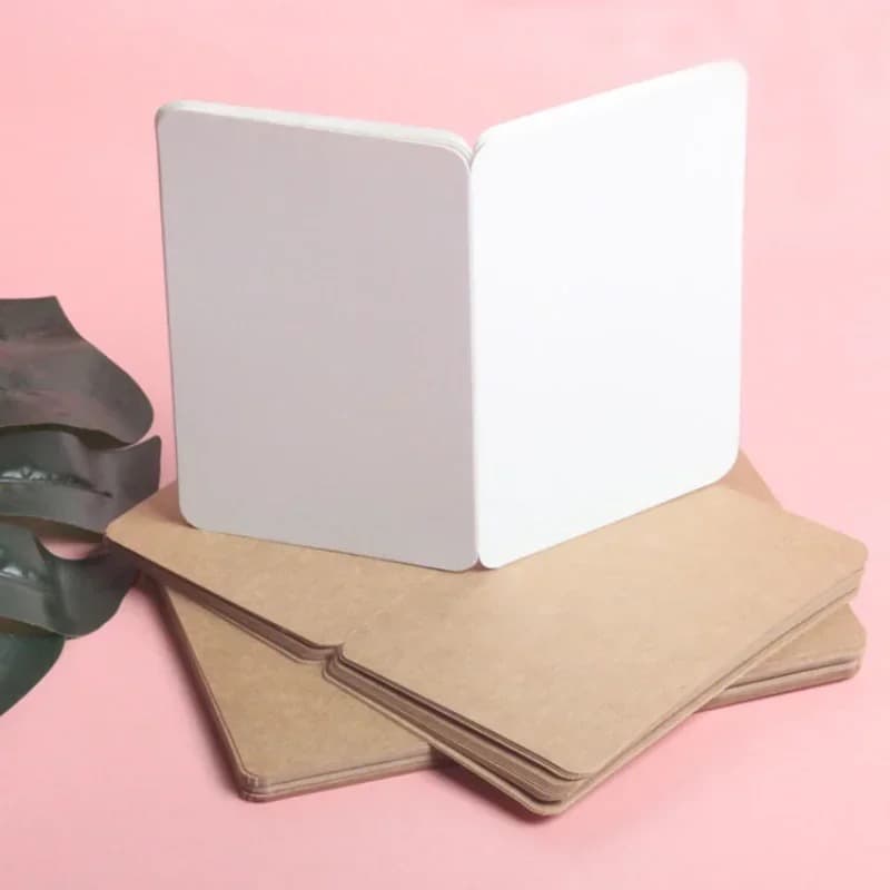 Carte pliée vierge posée debout sur une pile d'enveloppes kraft, sur fond rose.