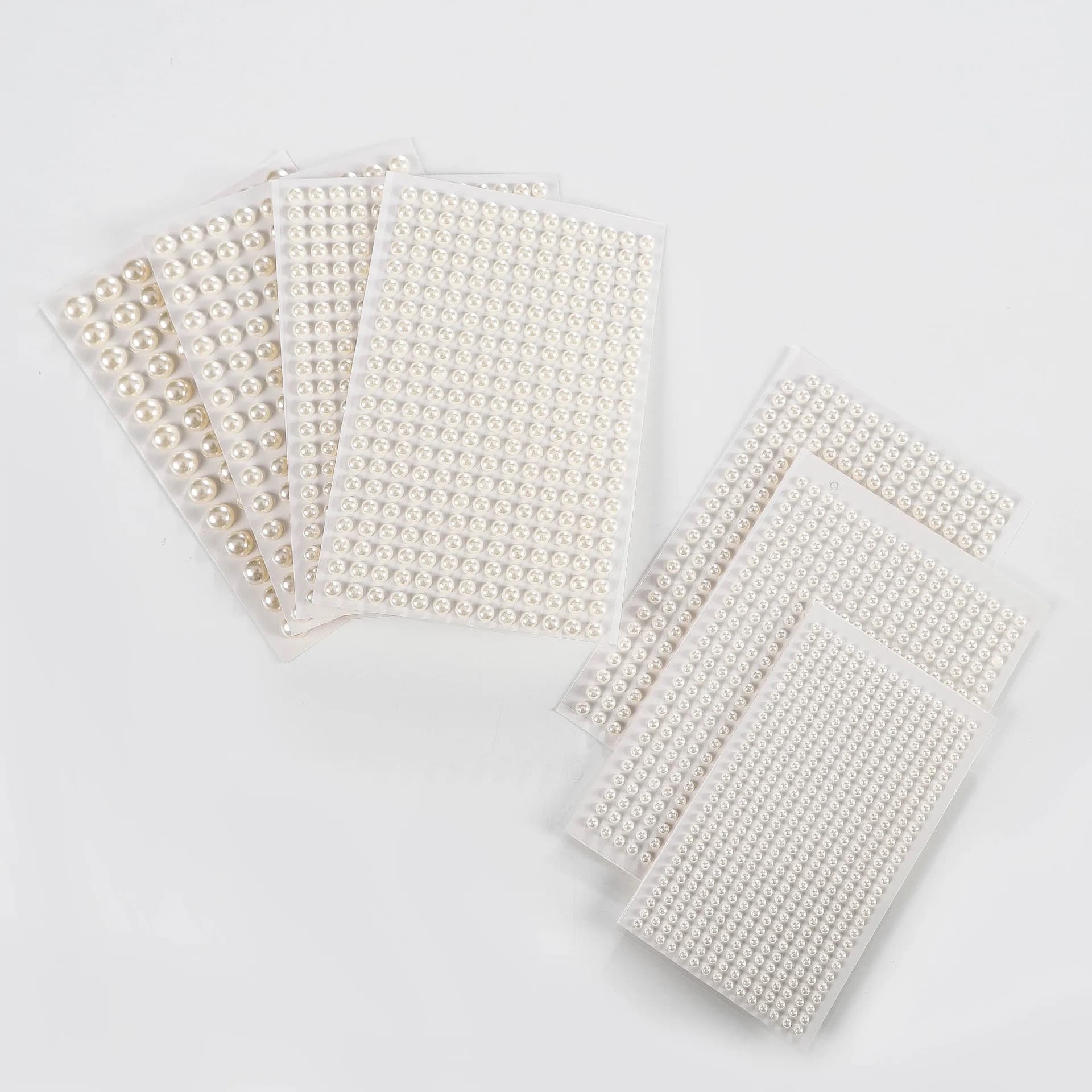 Planches transparentes de demi-perles blanches nacrées de différents diamètres, disposées en deux éventails sur fond clair.