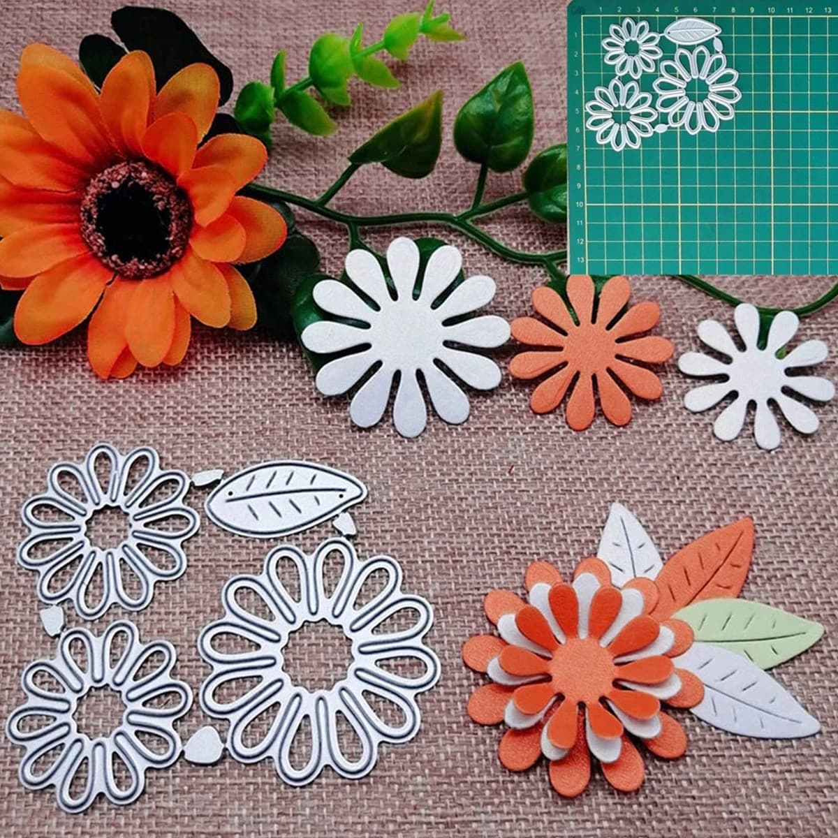 Quatre matrices de marguerites et une matrice de feuille posées sur une toile de jute, avec des découpes blanches, orange et vertes assemblées à côté.