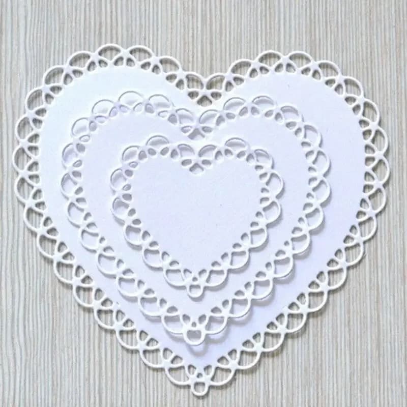 Trois coeurs en papier blanc de tailles différentes, bordés d'une dentelle d'anneaux, posés les uns sur les autres sur un plan de bois clair.