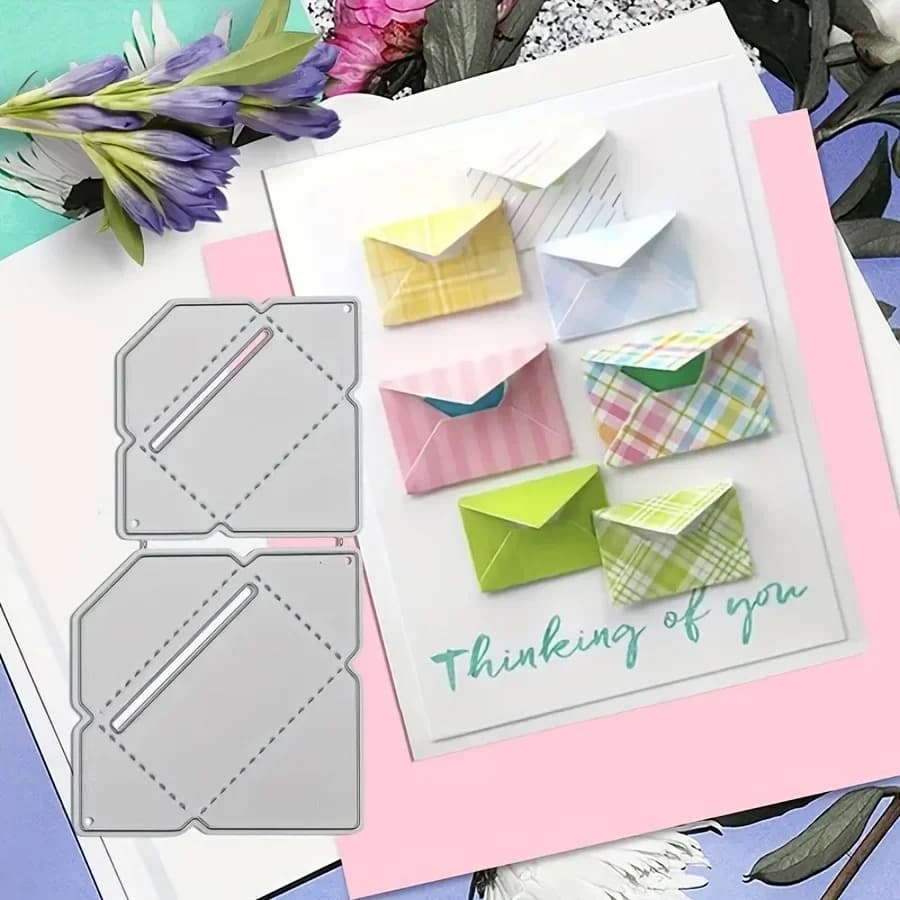 Deux matrices d'enveloppe en métal posées à côté d'une carte blanche sur laquelle six mini enveloppes pastel sont collées.