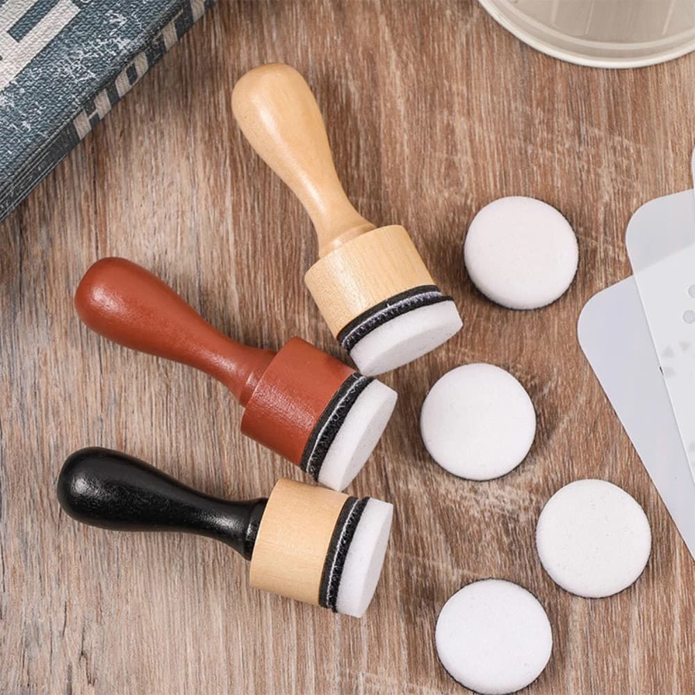 Trois applicateurs à manche en bois clair, acajou et noir, munis de coussins ronds blancs, posés sur une table en bois avec quatre coussins de rechange.