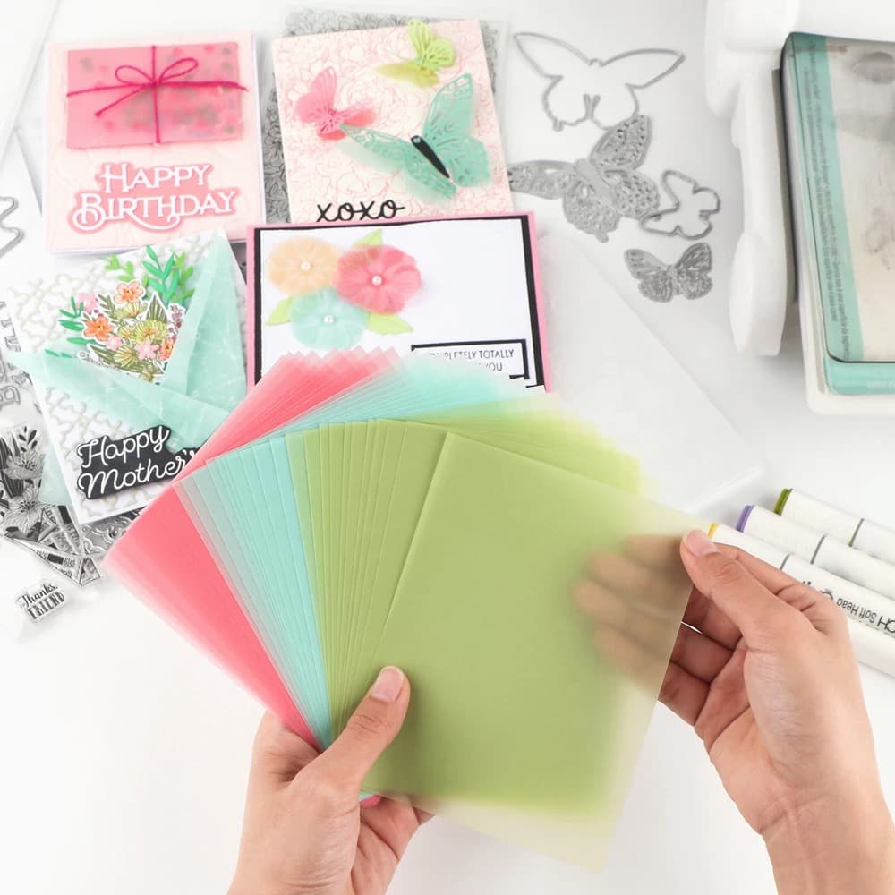 Eventail de feuilles de calque teintées rose, corail, menthe et vert tenues à deux mains devant des cartes terminées.