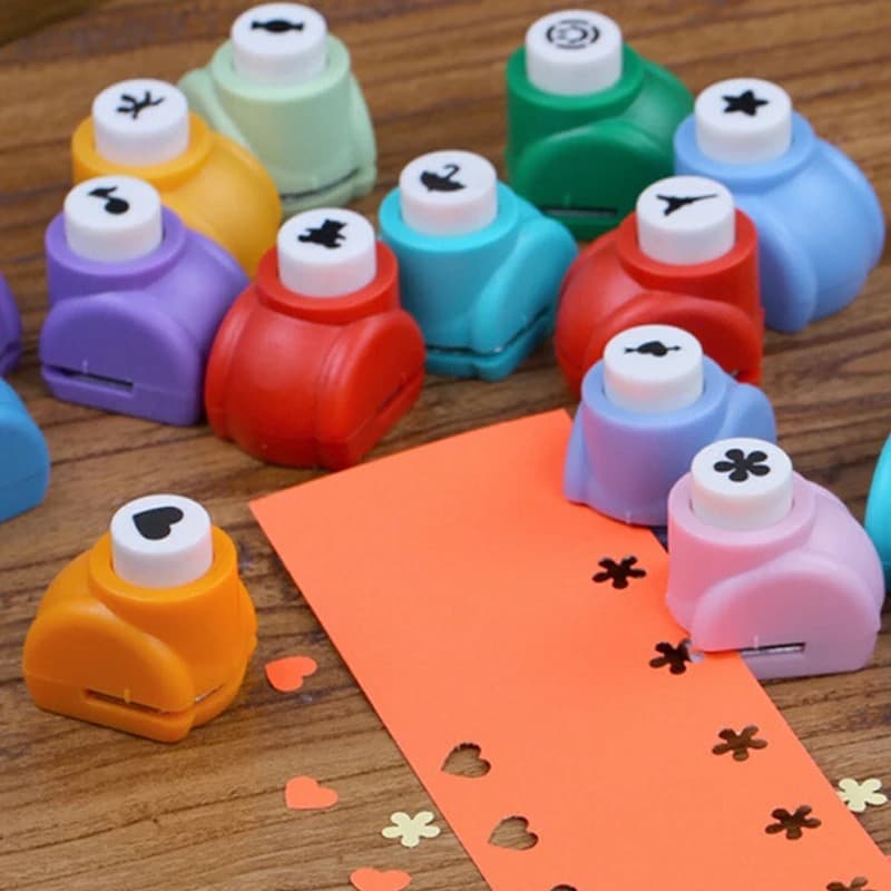 Mini perforatrices de couleurs variées posées sur un plan en bois, à côté d'une feuille de papier orange perforée de coeurs et de fleurs.