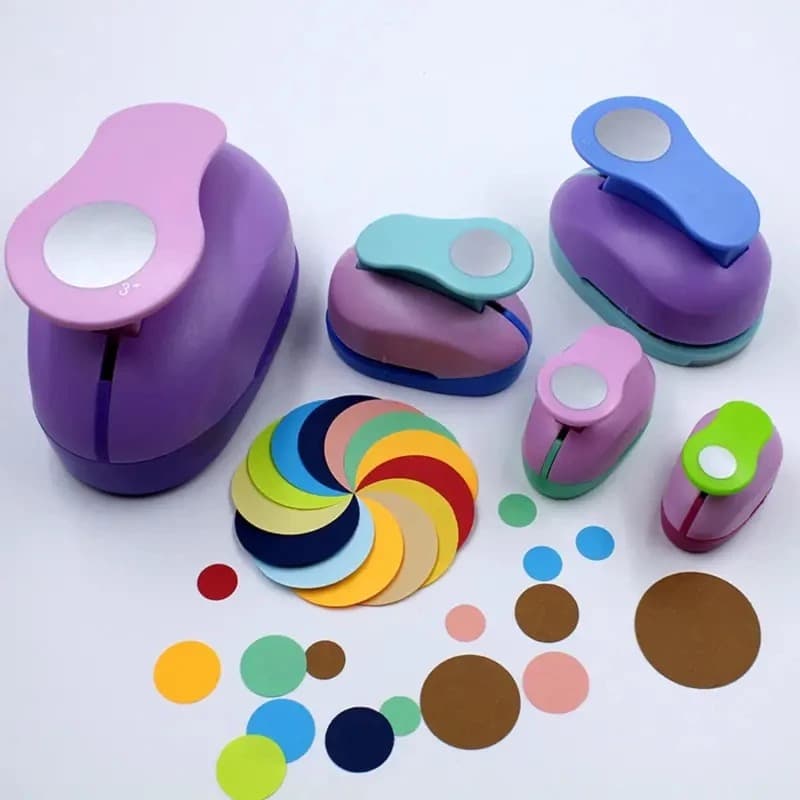 Cinq perforatrices à cercles de tailles différentes posées sur fond blanc, entourées des pastilles de papier découpées.