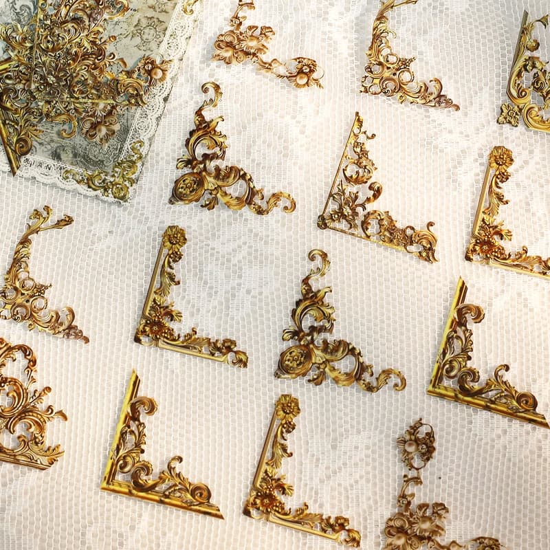 Autocollants d'angle dorés à volutes baroques, alignés sur un fond de dentelle blanche.