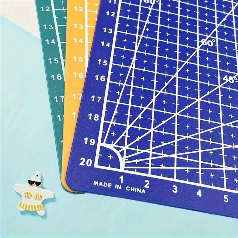 Tapis de découpe bleu quadrillé de blanc avec repères d'angles et graduations, posé sur deux autres tapis vert et orange.