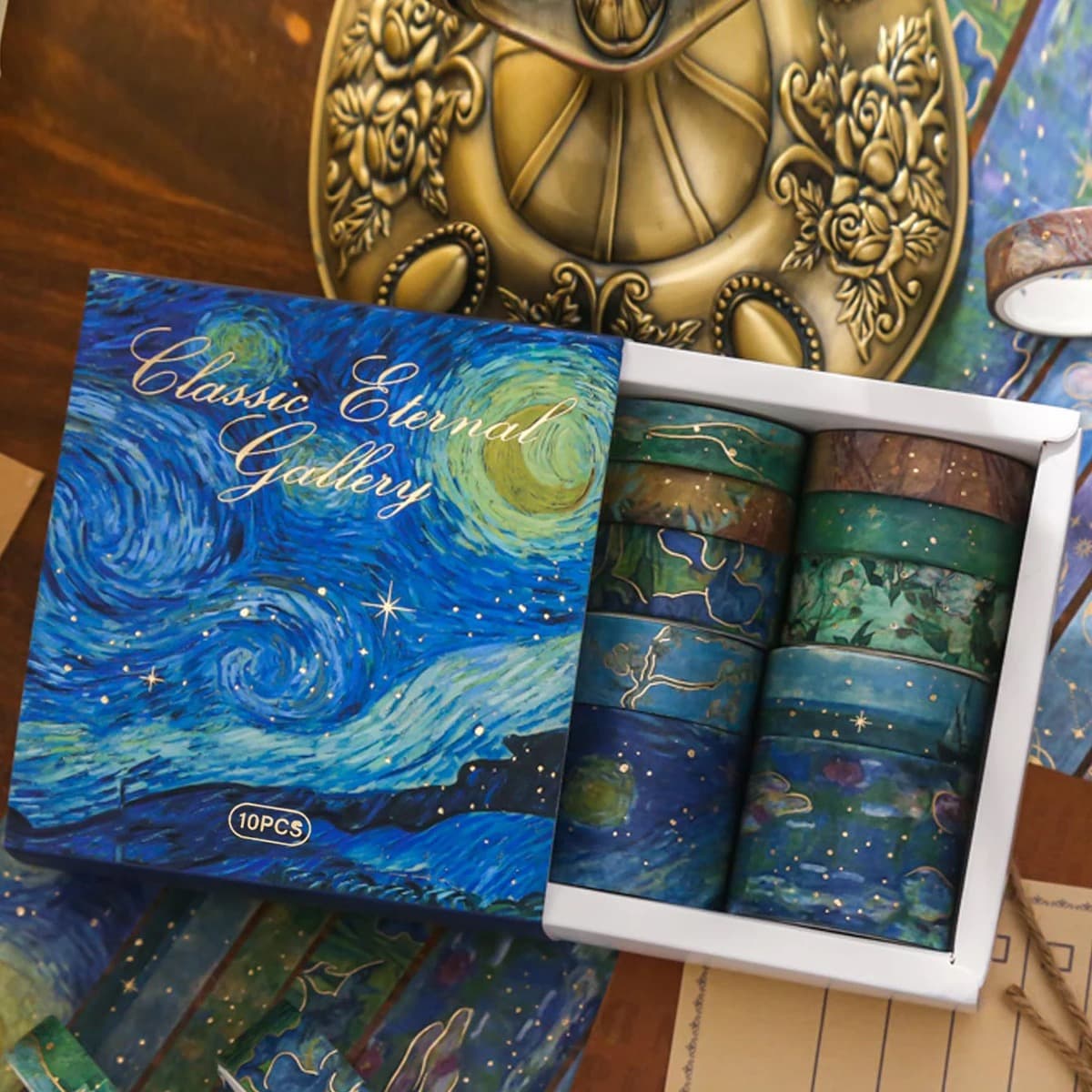 Coffret ouvert contenant dix rouleaux de washi tape aux motifs peints bleus et verts, posé sur une table en bois.