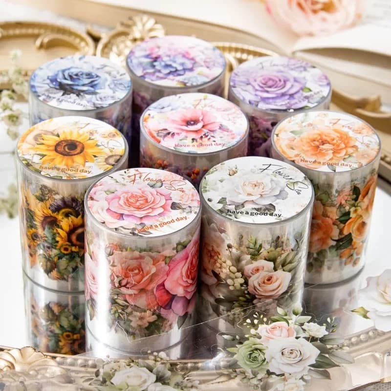 Rouleaux de washi tape à motifs floraux empilés sur un plateau doré, étiquettes visibles sur le dessus des bobines.